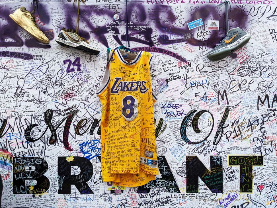 Memorial wall covered in graffiti messages with Lakers jersey number 8 and basketball shoes hanging as tributes