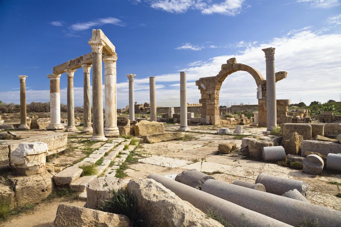 Ancient Roman ruins with stone columns, arches and scattered marble fragments under blue sky in Libya