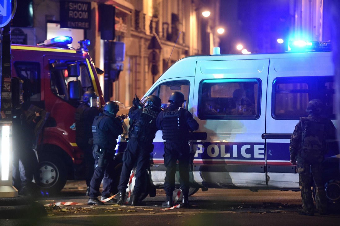 Armed police officers in tactical gear gathered around police vehicles with emergency lights during nighttime operation