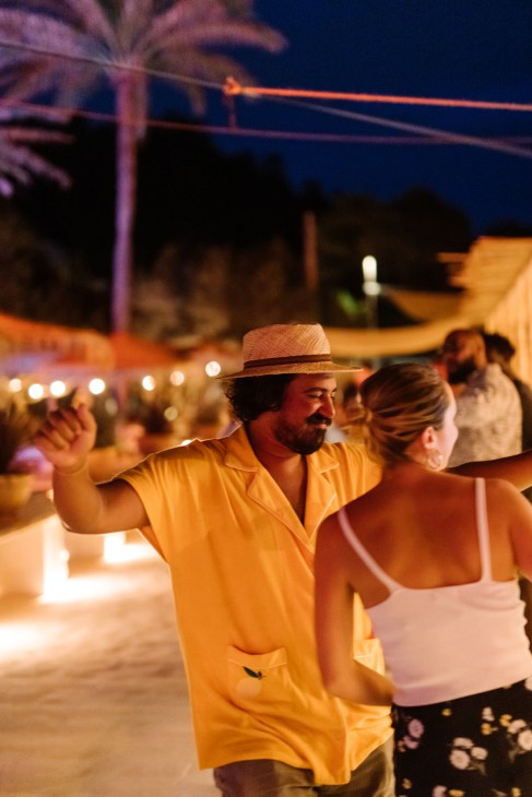 Man in yellow shirt and straw hat dancing with woman at beachside venue at night.