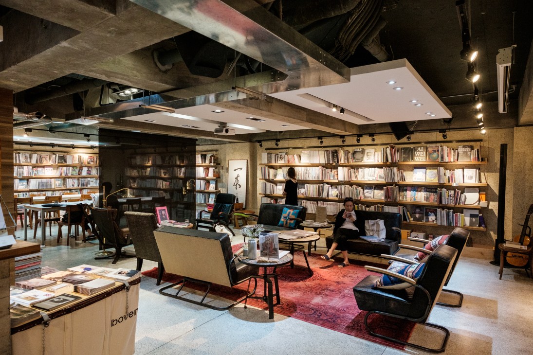 Modern bookstore interior with exposed ceiling, floor-to-ceiling bookshelves, and comfortable seating area