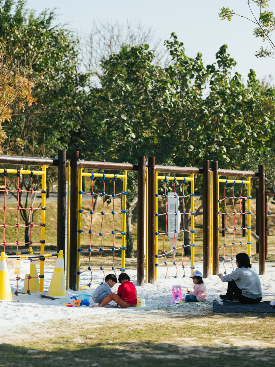 Adults and children sitting together at a colorful playground with rope climbing equipment