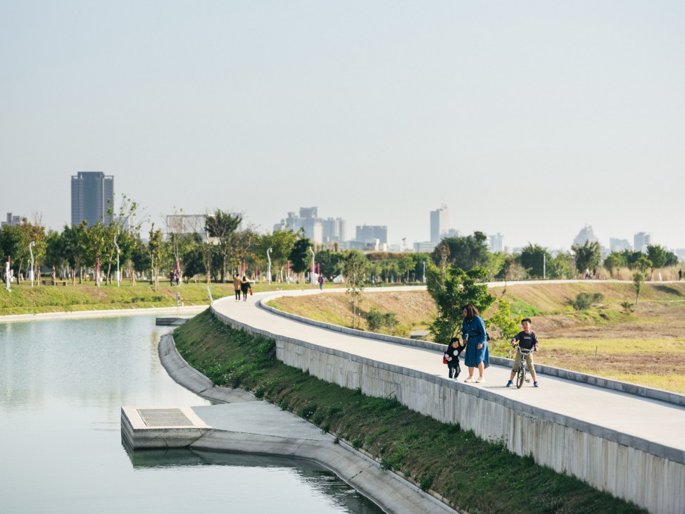 People walking along a curved concrete walkway beside a water channel in Taichung Central Park