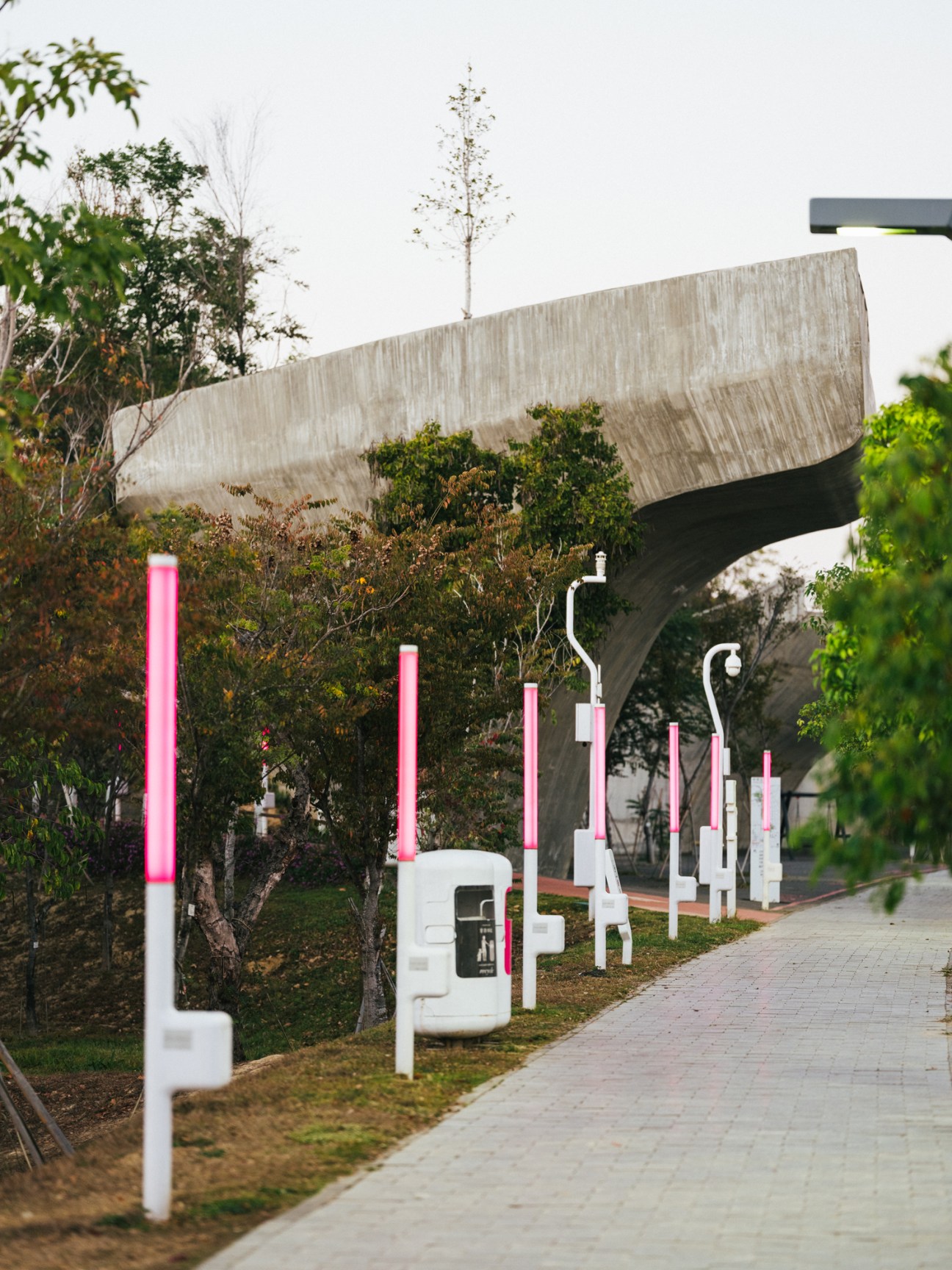 Pink and white charging stations lined up along a walkway near modern concrete architecture