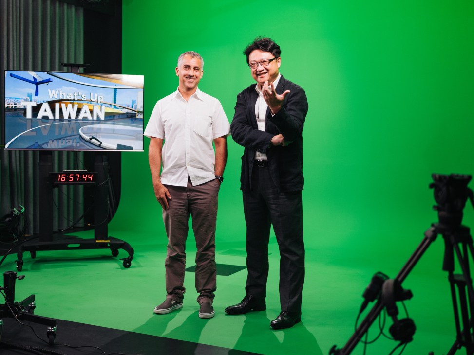 Two men stand on a green screen set with TaiwanPlus branding visible on a monitor.