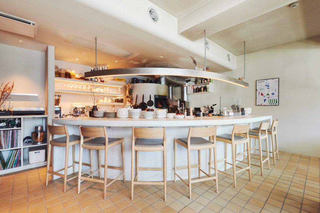 Interior of Songbook restaurant showing open kitchen with wood-fired oven and counter seating with wooden stools