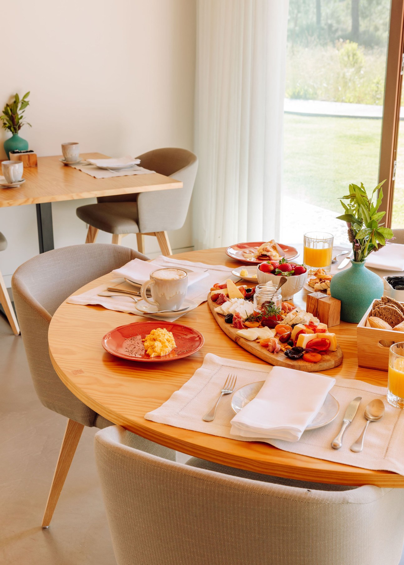 Breakfast table set with fresh food, coffee, juice and pastries on wooden round table by large window