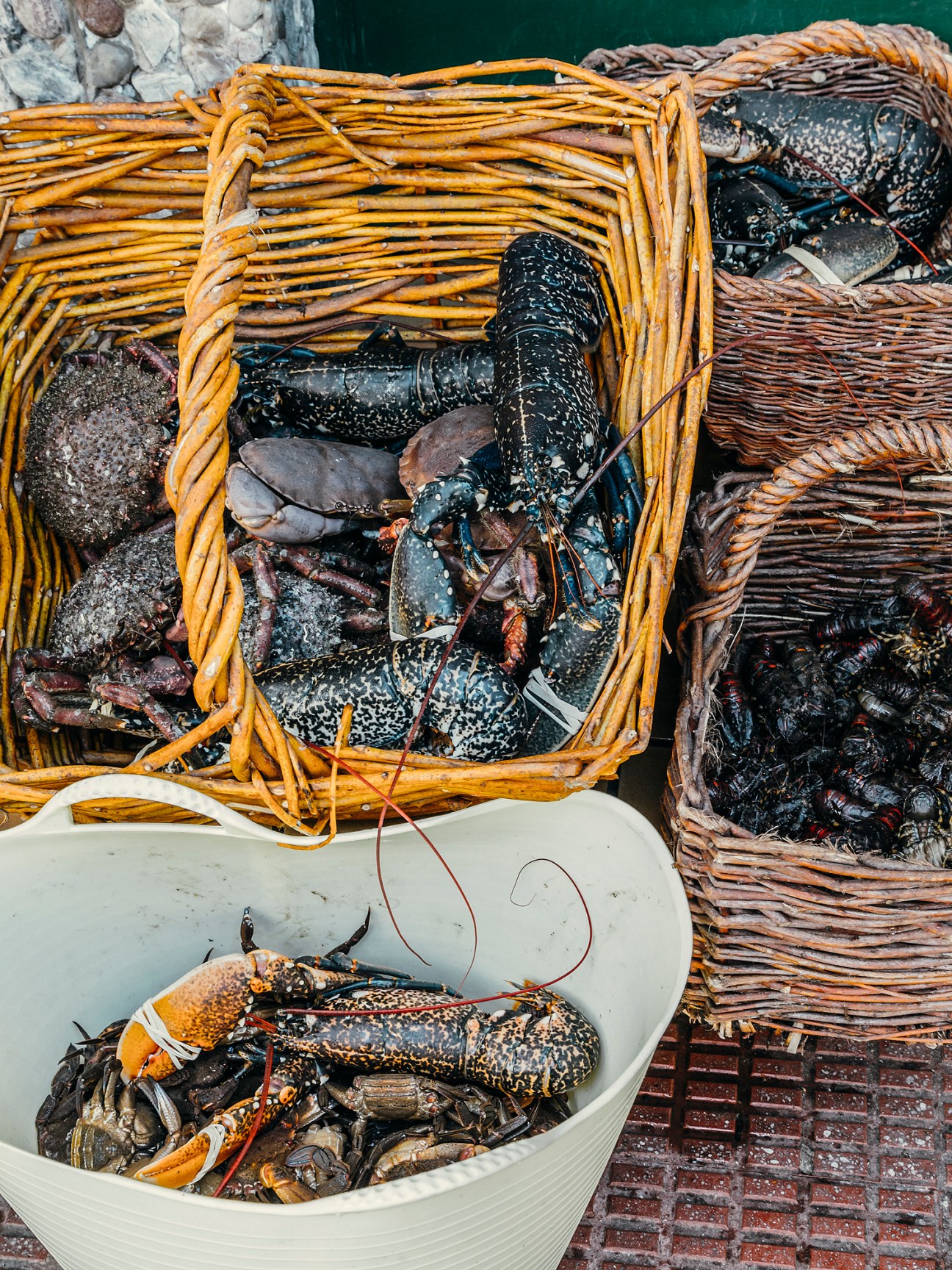 Fresh lobsters and crustaceans in woven baskets and a white bowl at a fishing port.