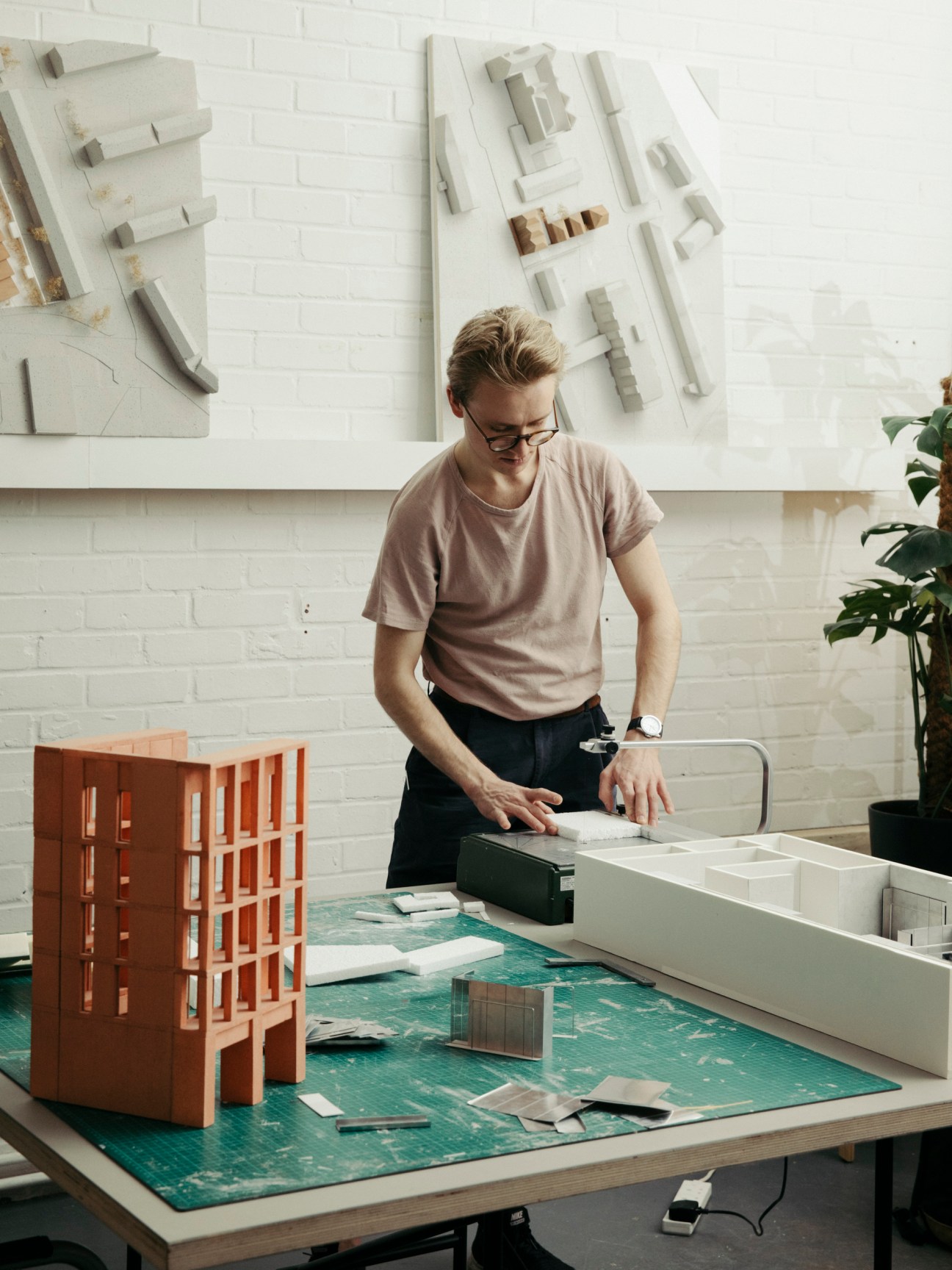Person examining detailed white architectural model on green cutting mat in design studio