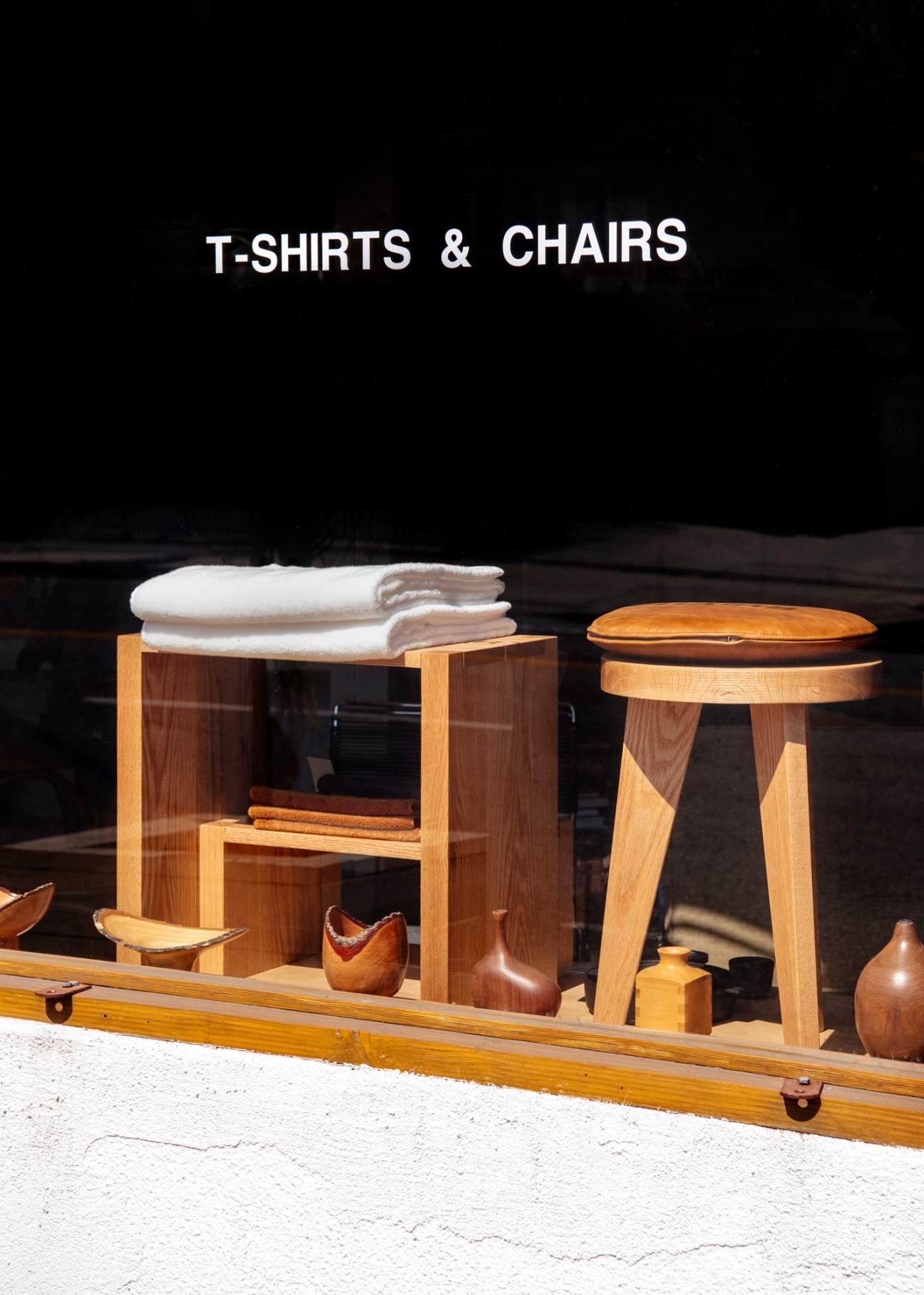 County Ltd shopfront window display with wooden furniture, folded white t-shirts, and signage reading 'T-SHIRTS & CHAIRS'