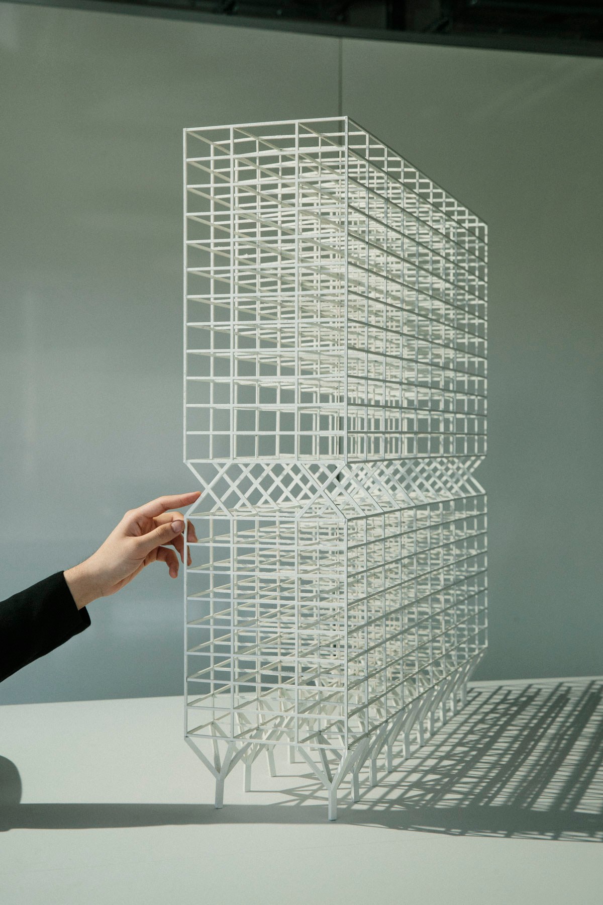 White skeletal architectural model showing grid-like framework structure with hand reaching toward it