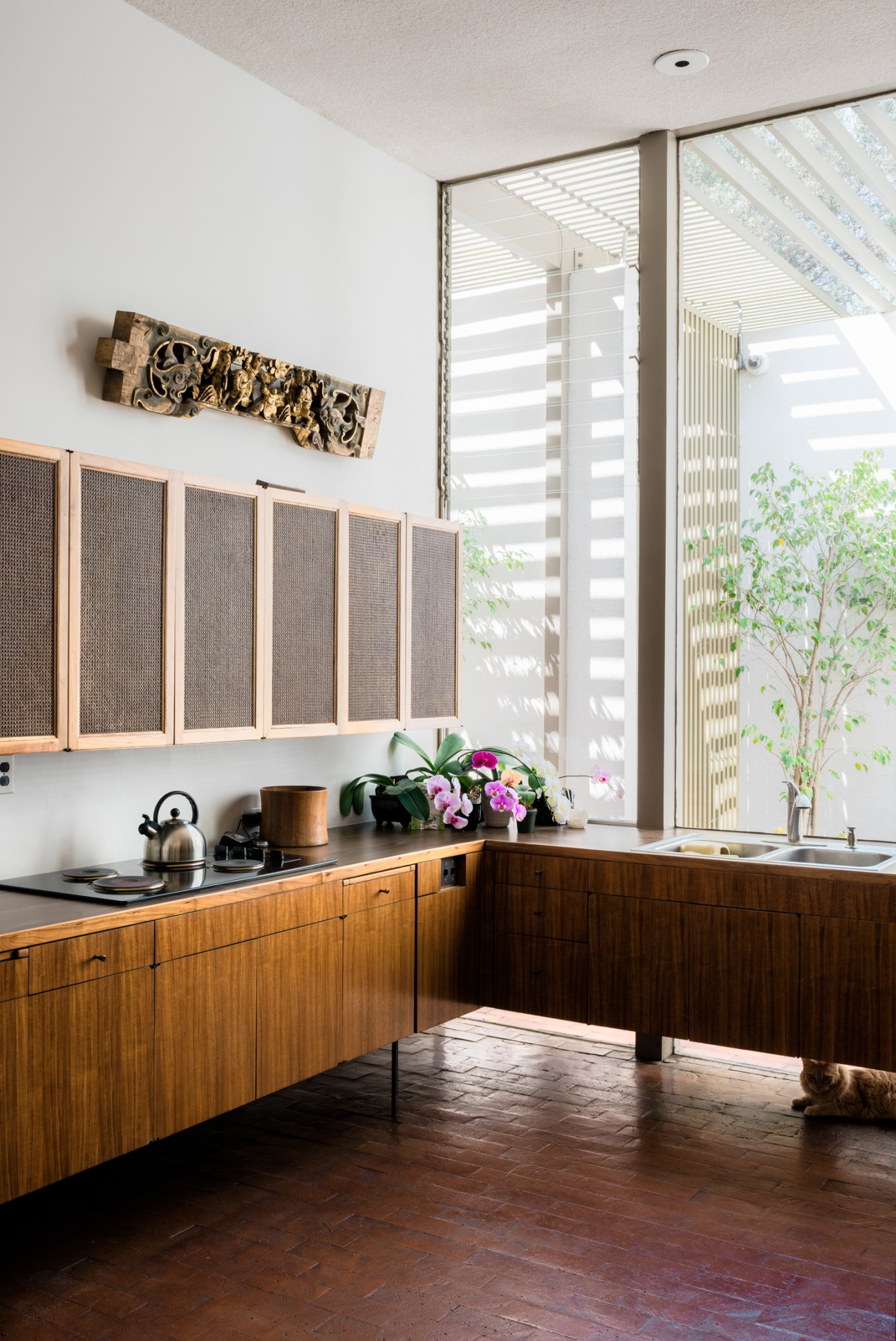 Mid-century modern kitchen with wooden cabinetry, mesh-front upper cabinets, and large glass doors opening to an outdoor courtyard with pergola.