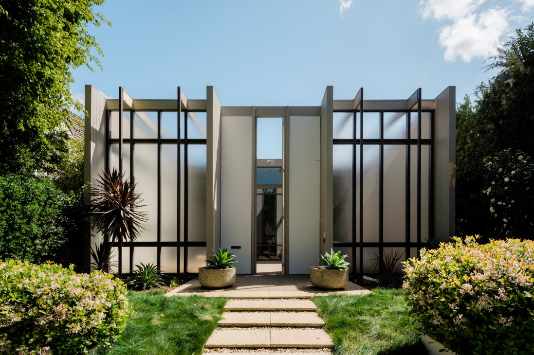Mid-century modern house with large grid-pattern doors and frosted glass panels flanked by landscaped gardens.