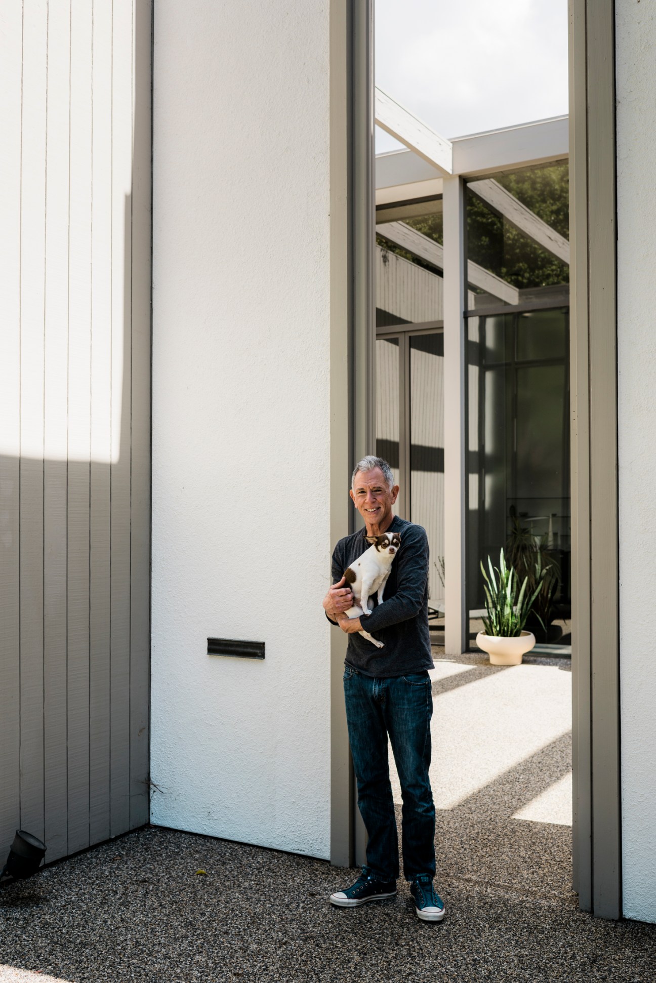 Brady House owner Lewy Kallas holding his small white and brown dog Moxie in a minimalist mid-century modern entryway.