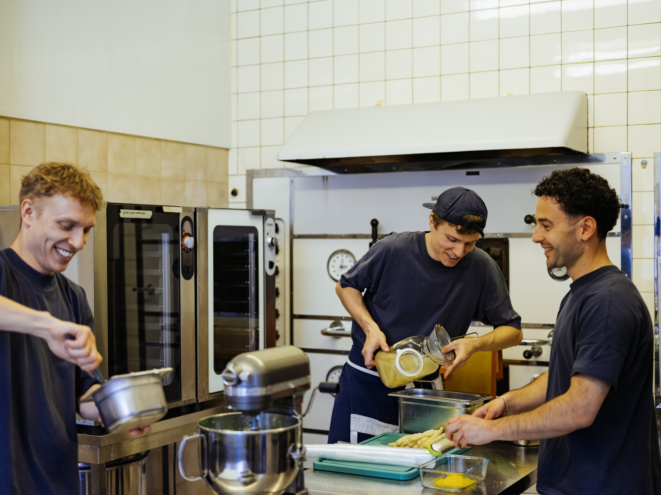 Three males preparing food in a kitchen.
