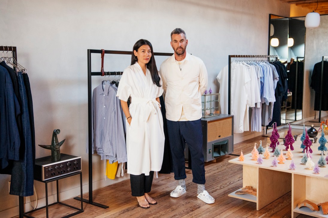 Bo and Kevin Carney stand in their Smock shop surrounded by clothing racks and colorful decorative objects.