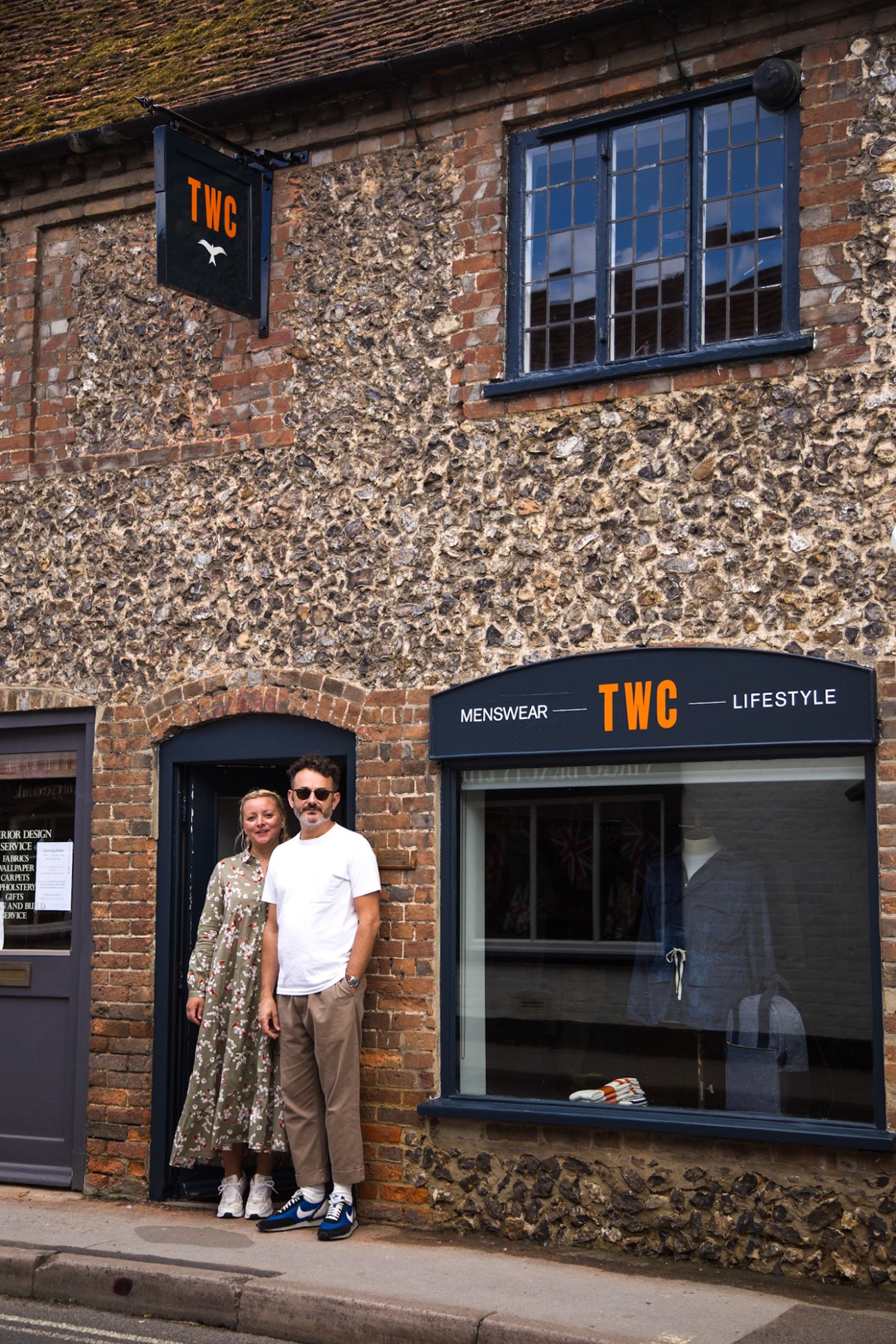 Two people standing in the doorway of The Workers Club (TWC) menswear and lifestyle shop with ivy-covered brick facade.
