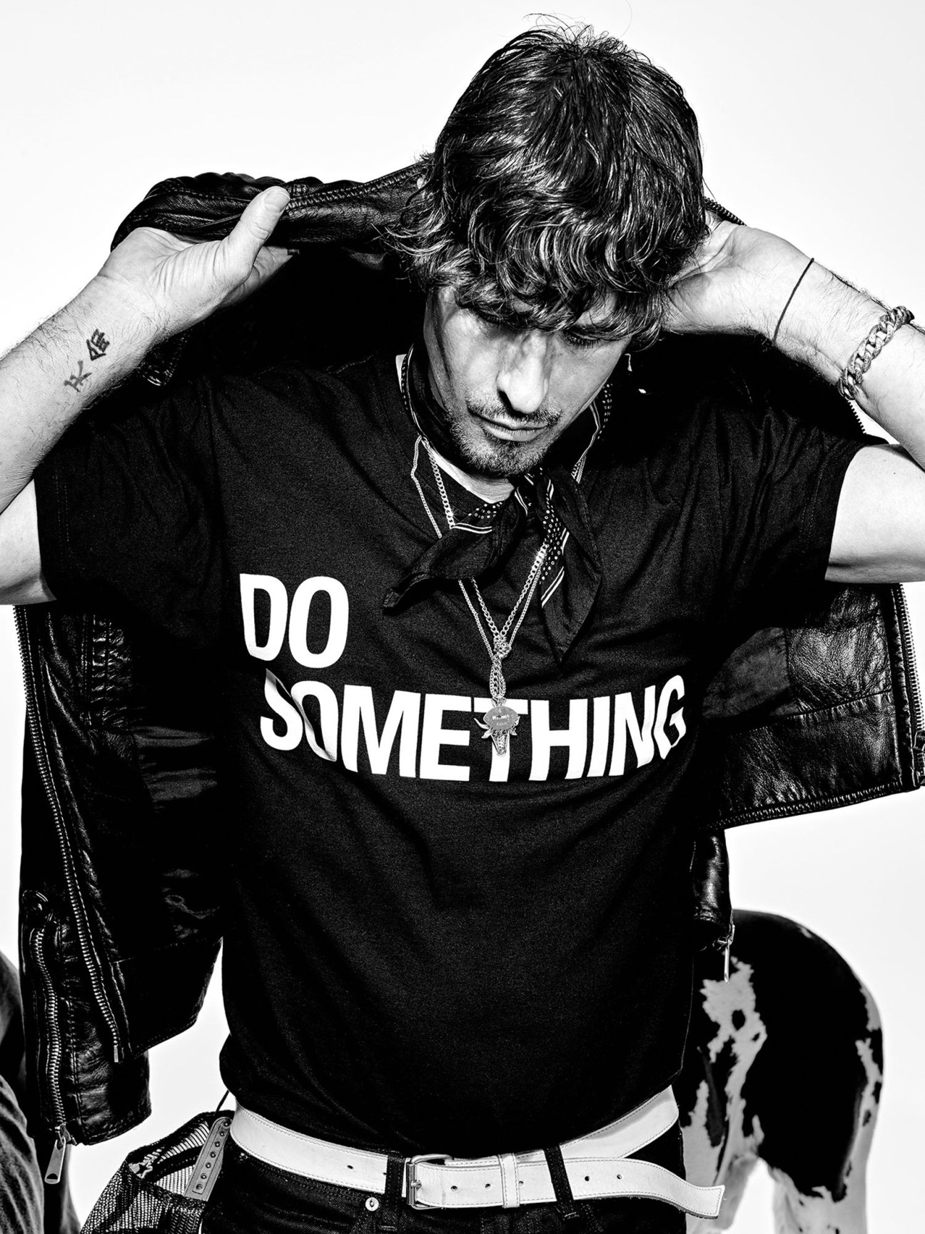 Black and white portrait of photographer Steven Klein wearing a t-shirt that says 'DO SOMETHING' and a leather jacket