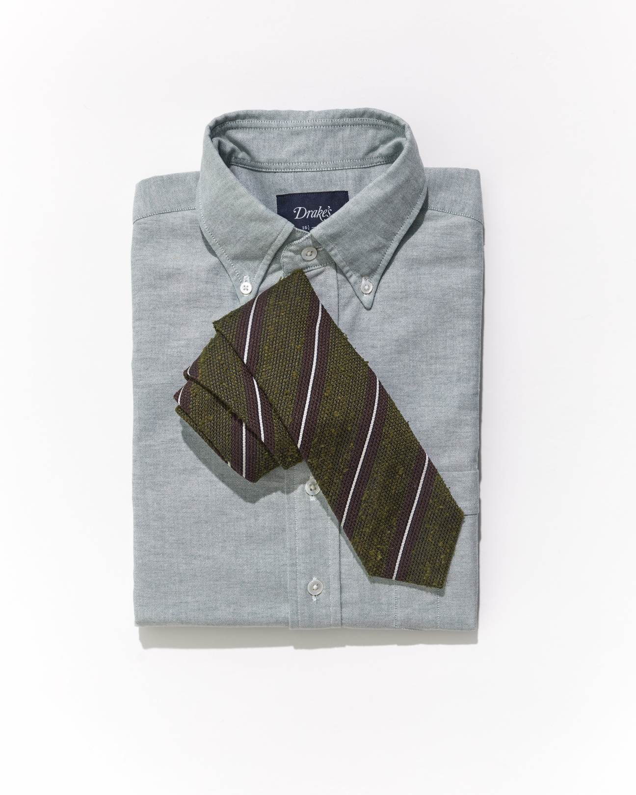Olive green tie with diagonal stripes laid on light gray dress shirt