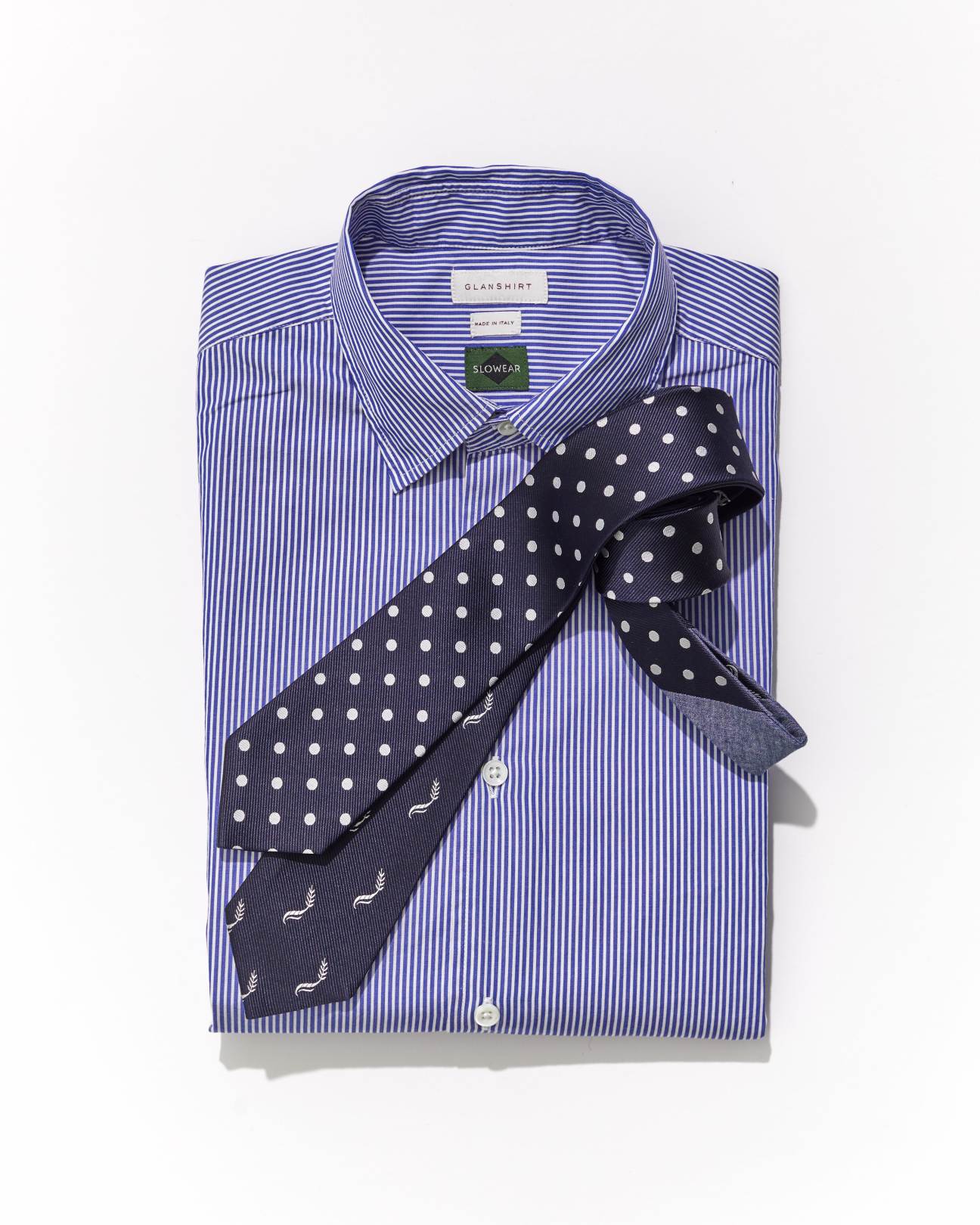 Navy polka dot tie laid across purple and white striped dress shirt