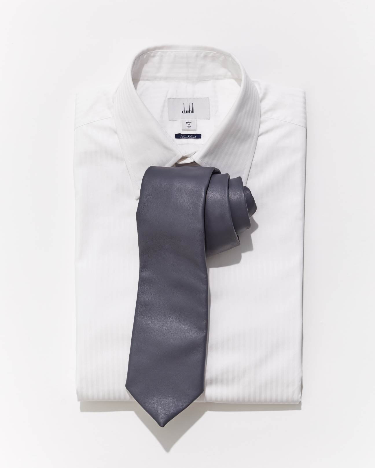 Gray necktie arranged on white dress shirt against neutral background
