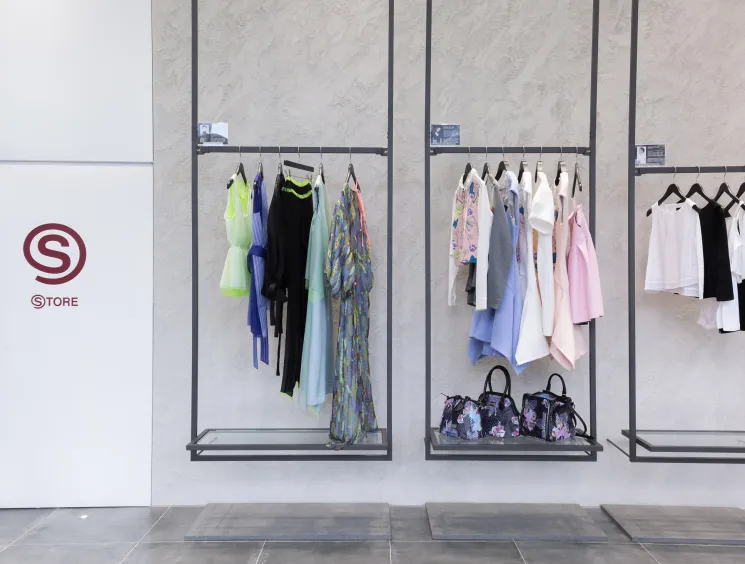 Minimalist fashion boutique interior with wall-mounted clothing racks displaying colourful garments and accessories beneath the S Store logo.