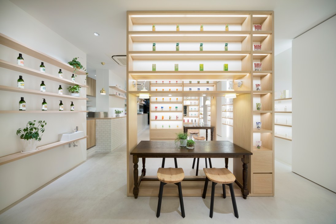 Modern retail interior with light wood shelving displaying products, a dark wooden table with wooden stools, and organized merchandise displays.