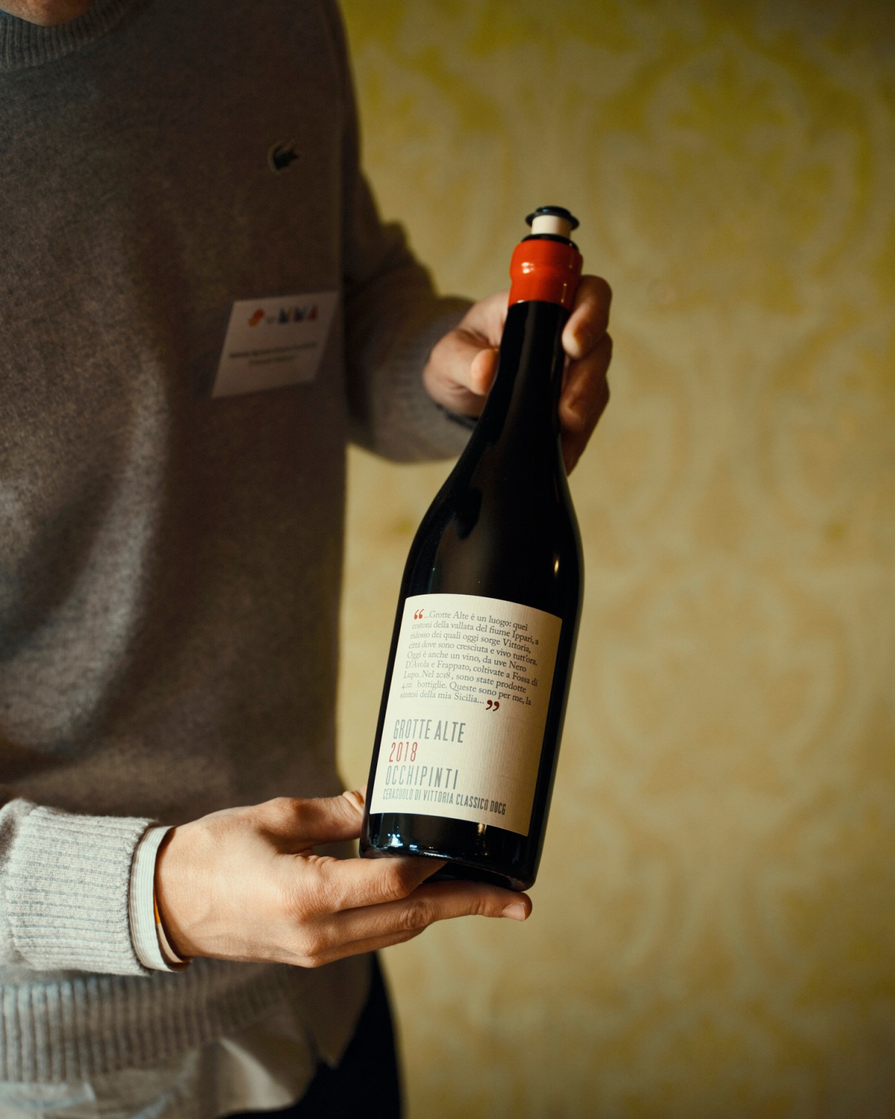 Hands holding a bottle of Grotte Alte 2018 Occhipinti wine with red wax seal and white label
