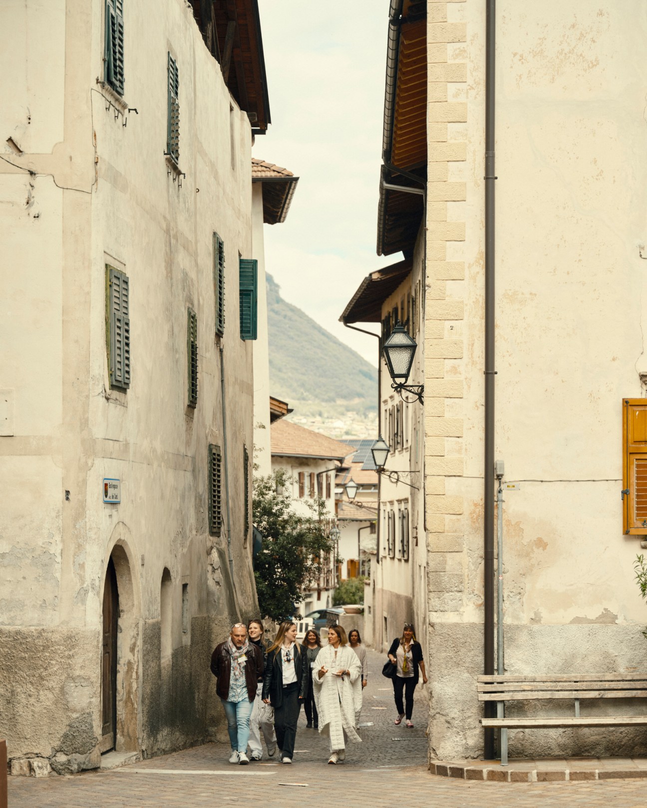 People walking down a narrow cobblestone street lined with historic stone buildings in Magrè