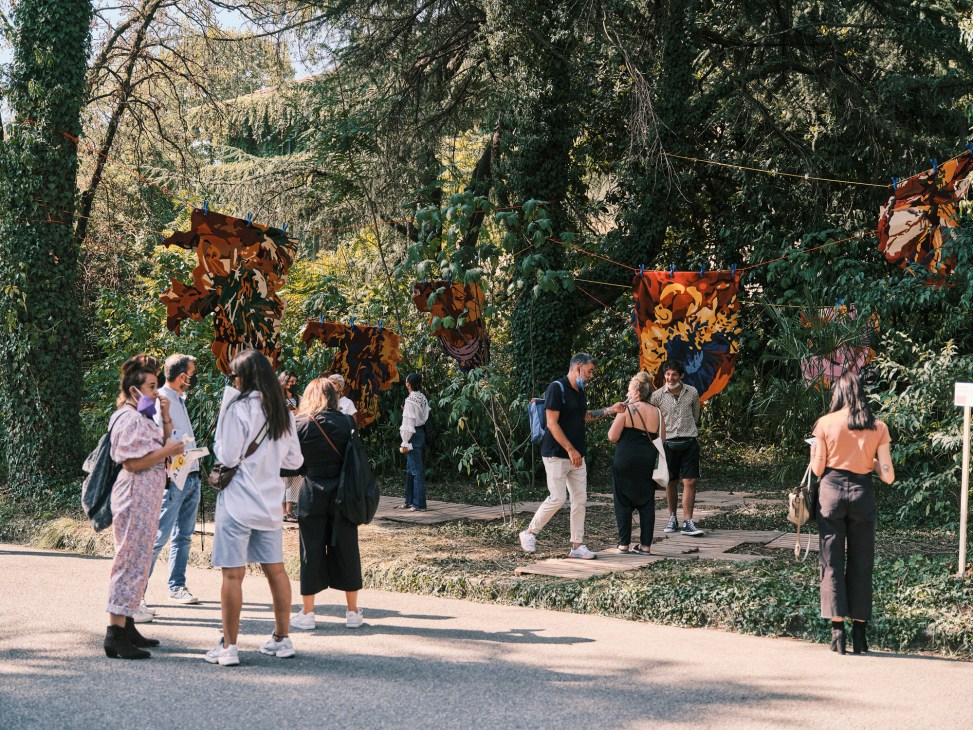Visitors exploring Alcova design exhibition in unconventional outdoor venue with hanging fabric installations among trees