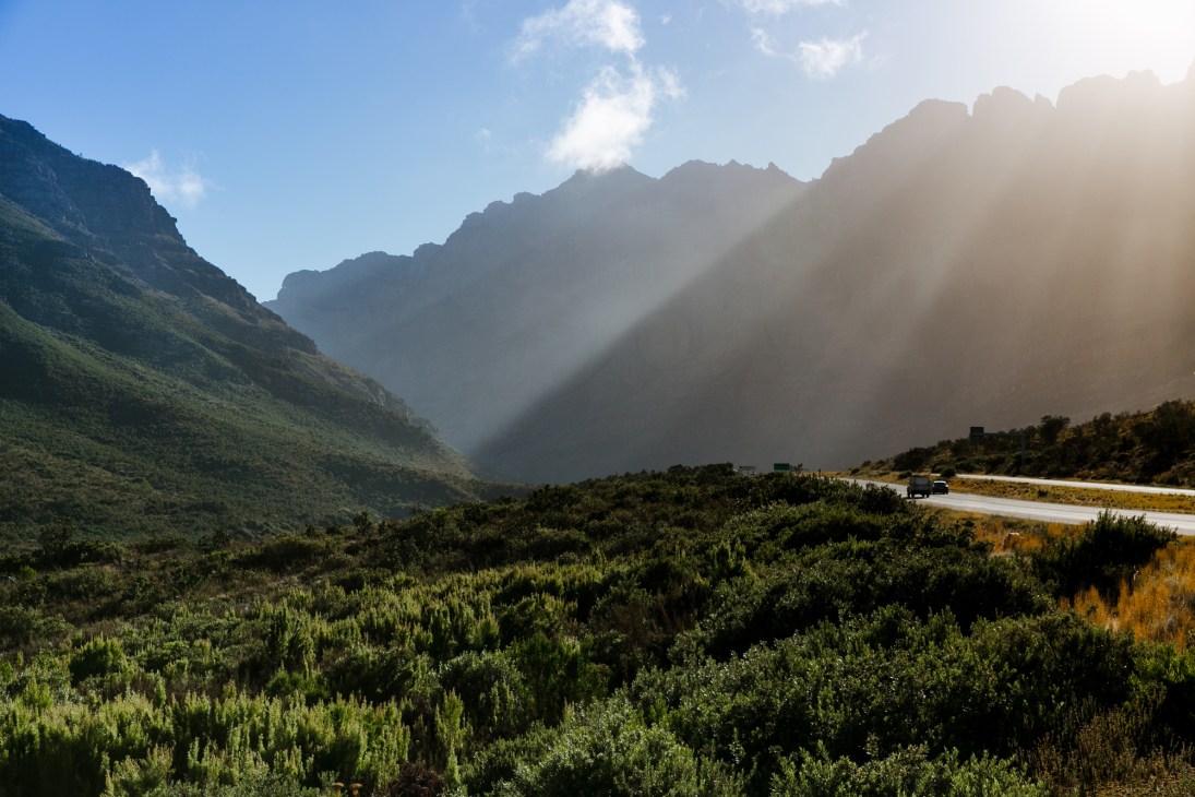 Winding mountain road through dramatic rocky peaks with sun rays filtering through the valley