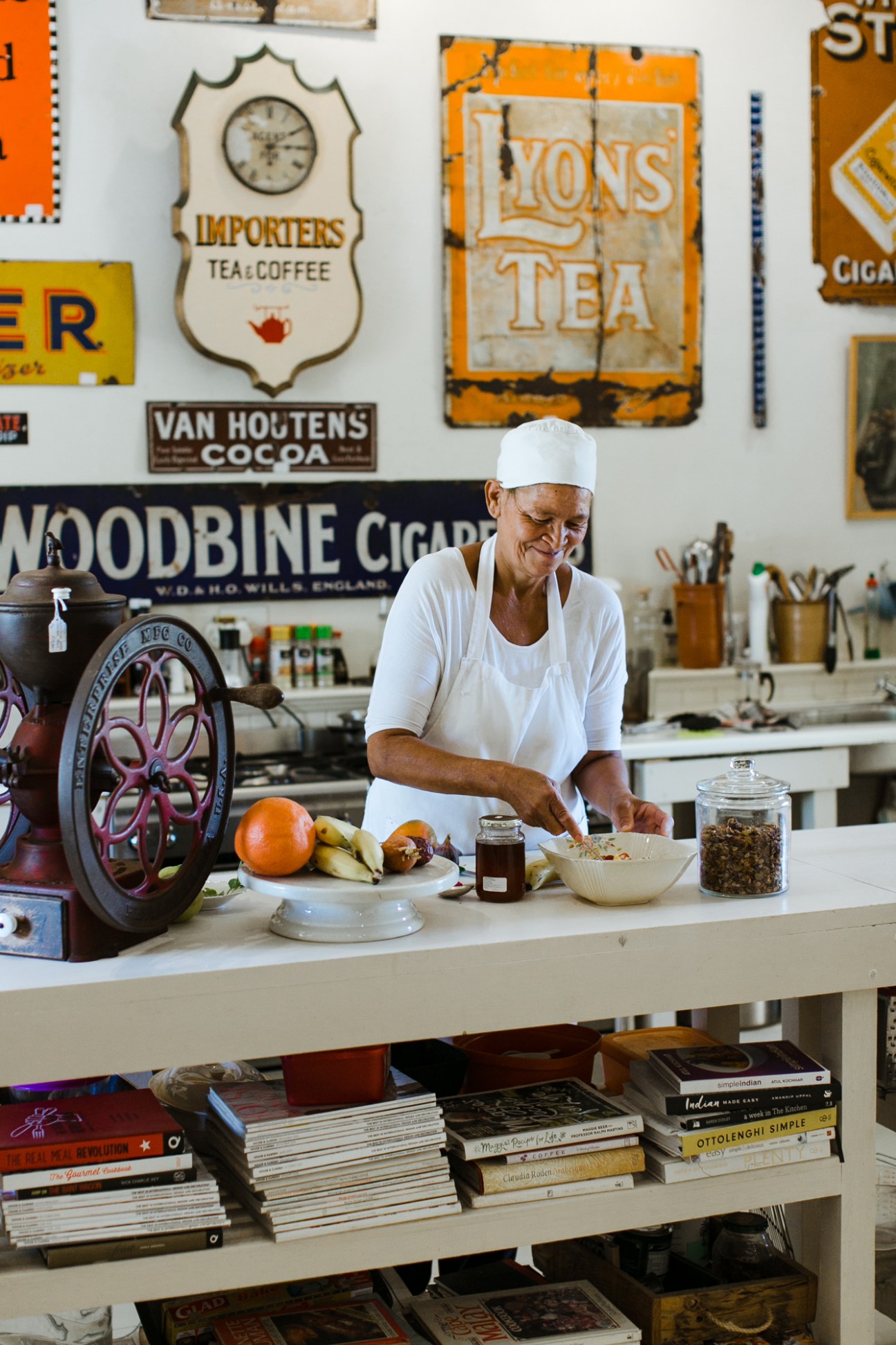 Woman in white chef's attire preparing breakfast at Prince Albert Country Stay with vintage kitchen signs on wall