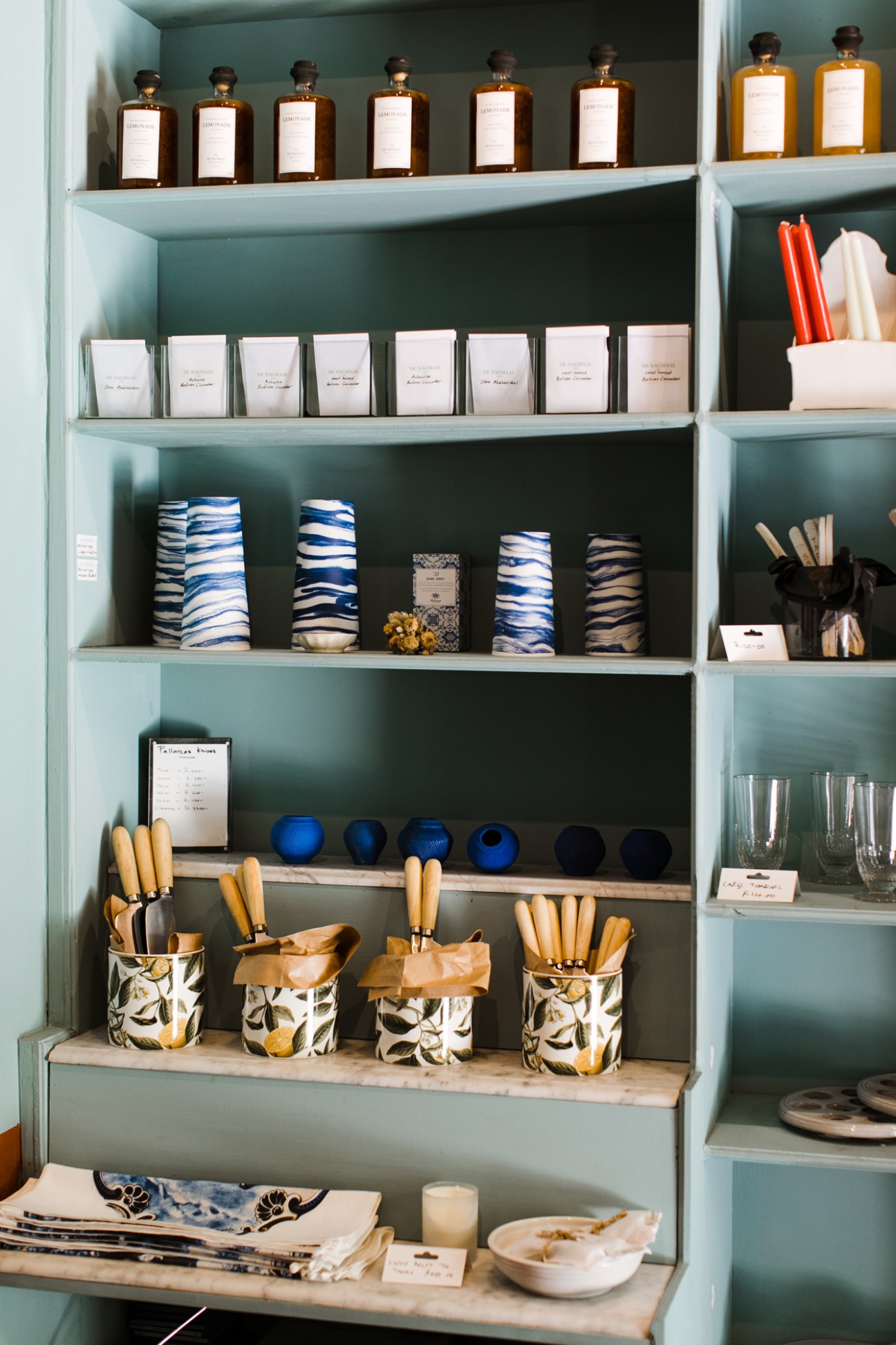 Organized shelves displaying bottles, ceramics, linens and crafts at De Nagmaal shop