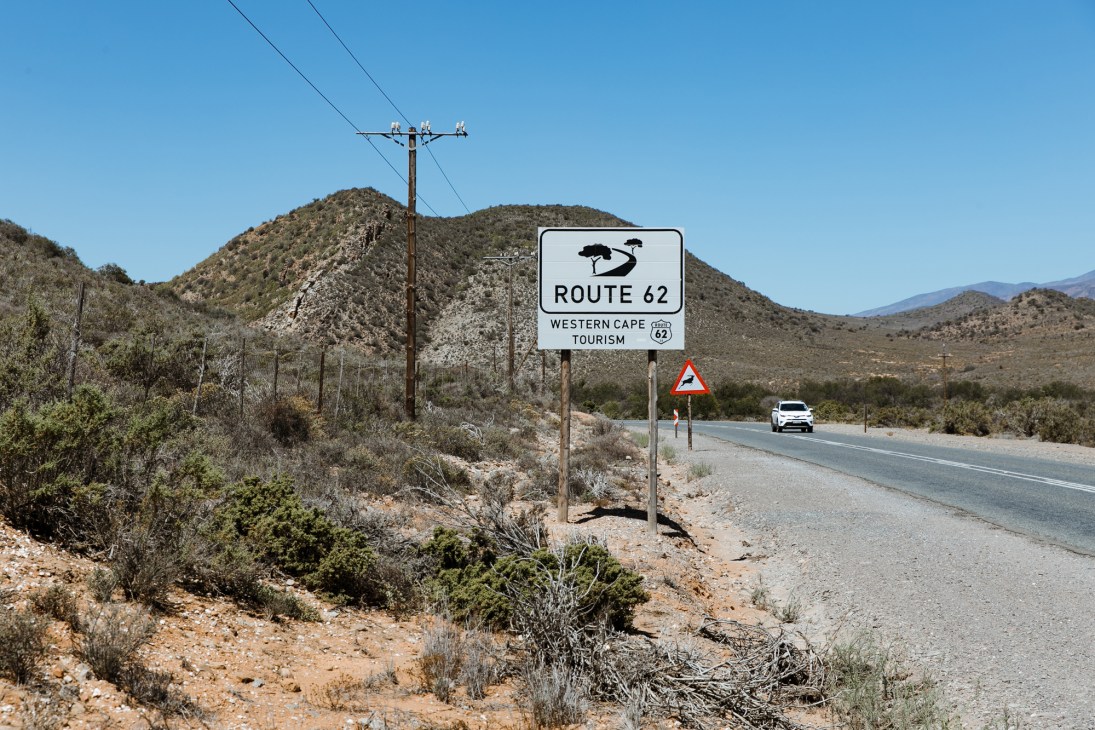 Route 62 road sign with baobab tree logo in arid South African landscape with hills and power lines