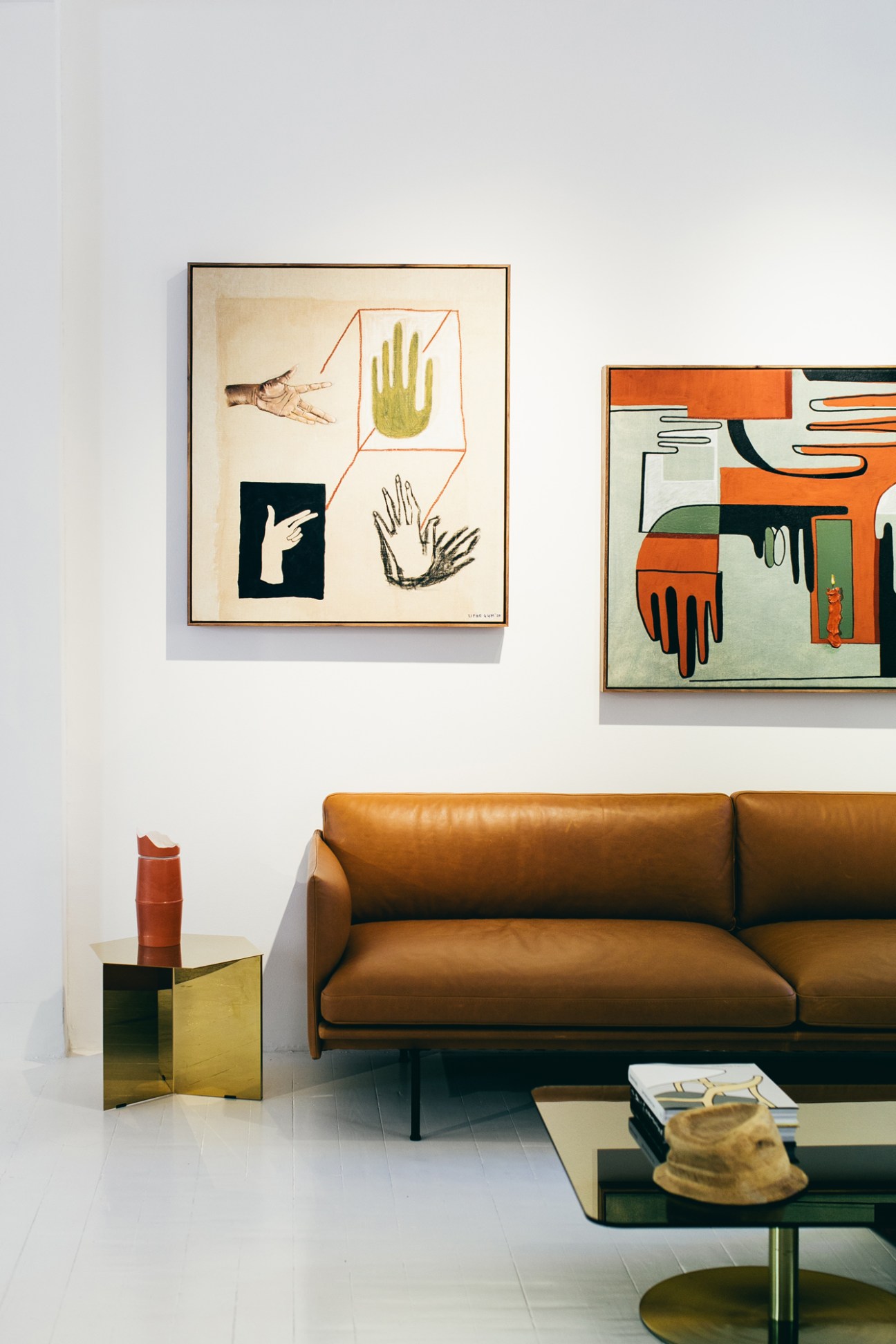Modern living room with tan leather sofa, framed hand artworks on white wall, and geometric side tables