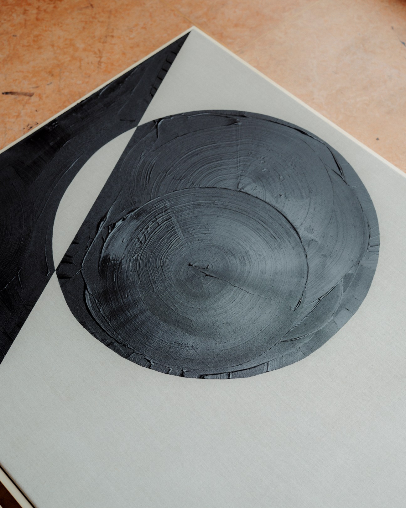 Abstract charcoal and marble artwork on white paper showing circular concentric patterns with bold black brushstrokes.