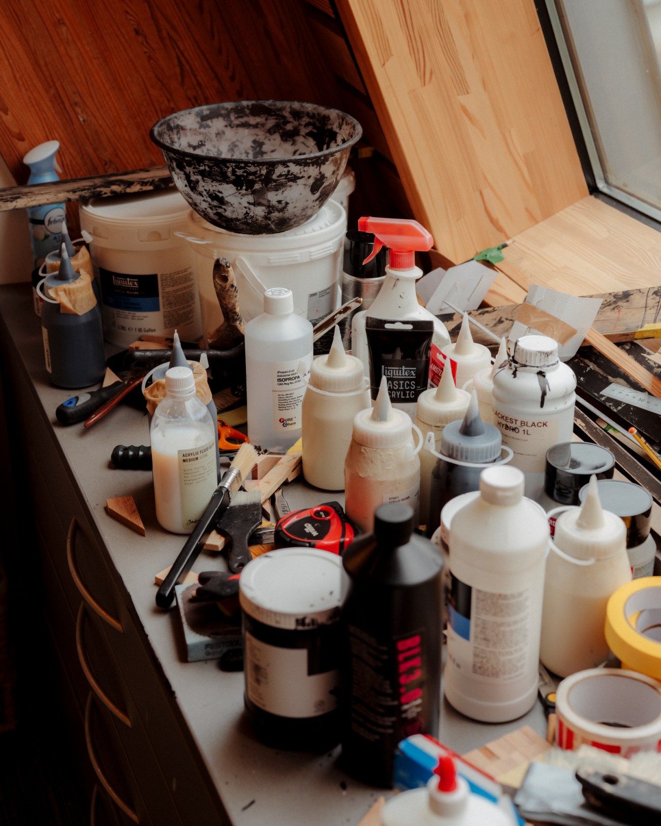 Artist's studio workspace with paint bottles, brushes, and a textured black ceramic bowl on wooden surfaces.