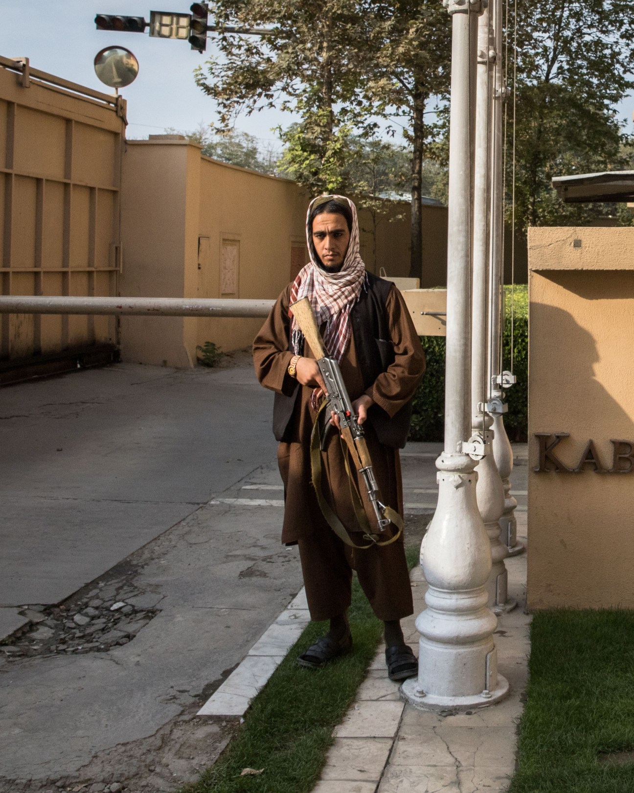 Taliban fighter with rifle and checkered headscarf standing guard outside hotel entrance