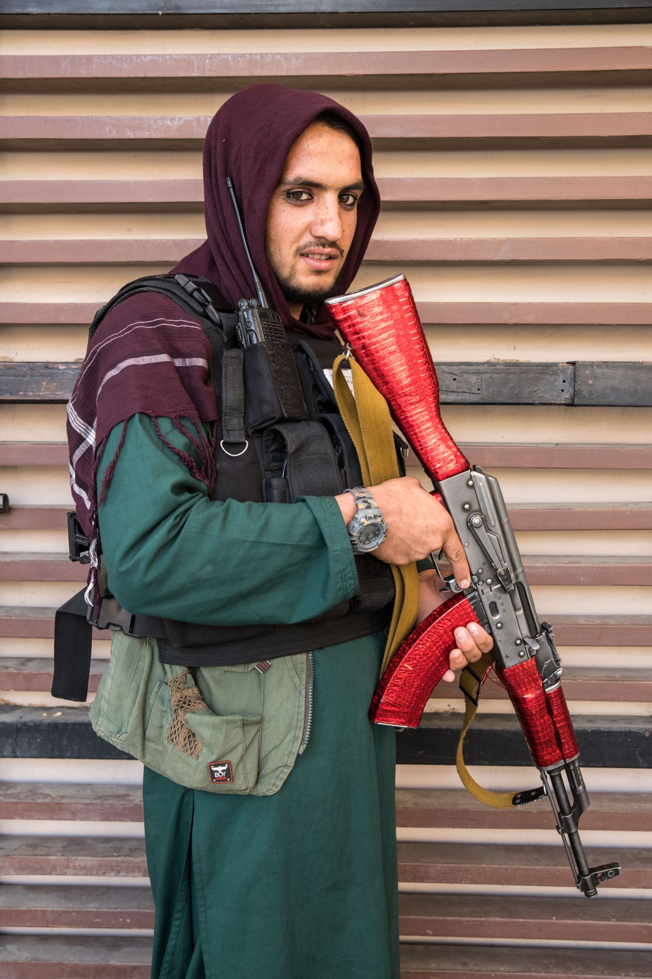 Taliban fighter in maroon hoodie holding assault rifle with red tape wrapped around stock