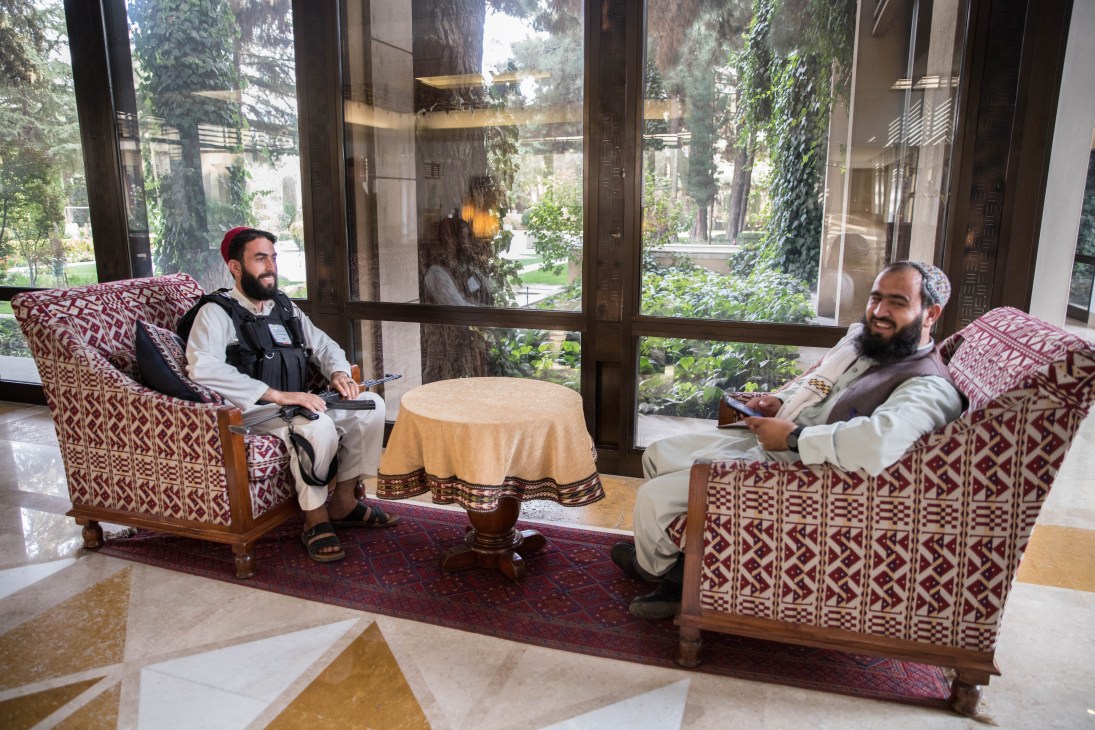Two bearded men in traditional clothing sitting in ornate patterned chairs in an upscale hotel lobby