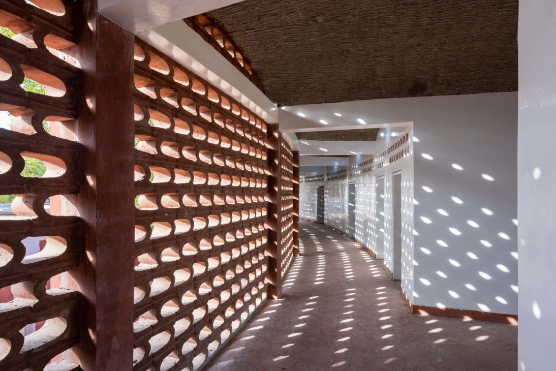 Perforated brick wall creating decorative light patterns in hospital corridor designed by Manuel Herz