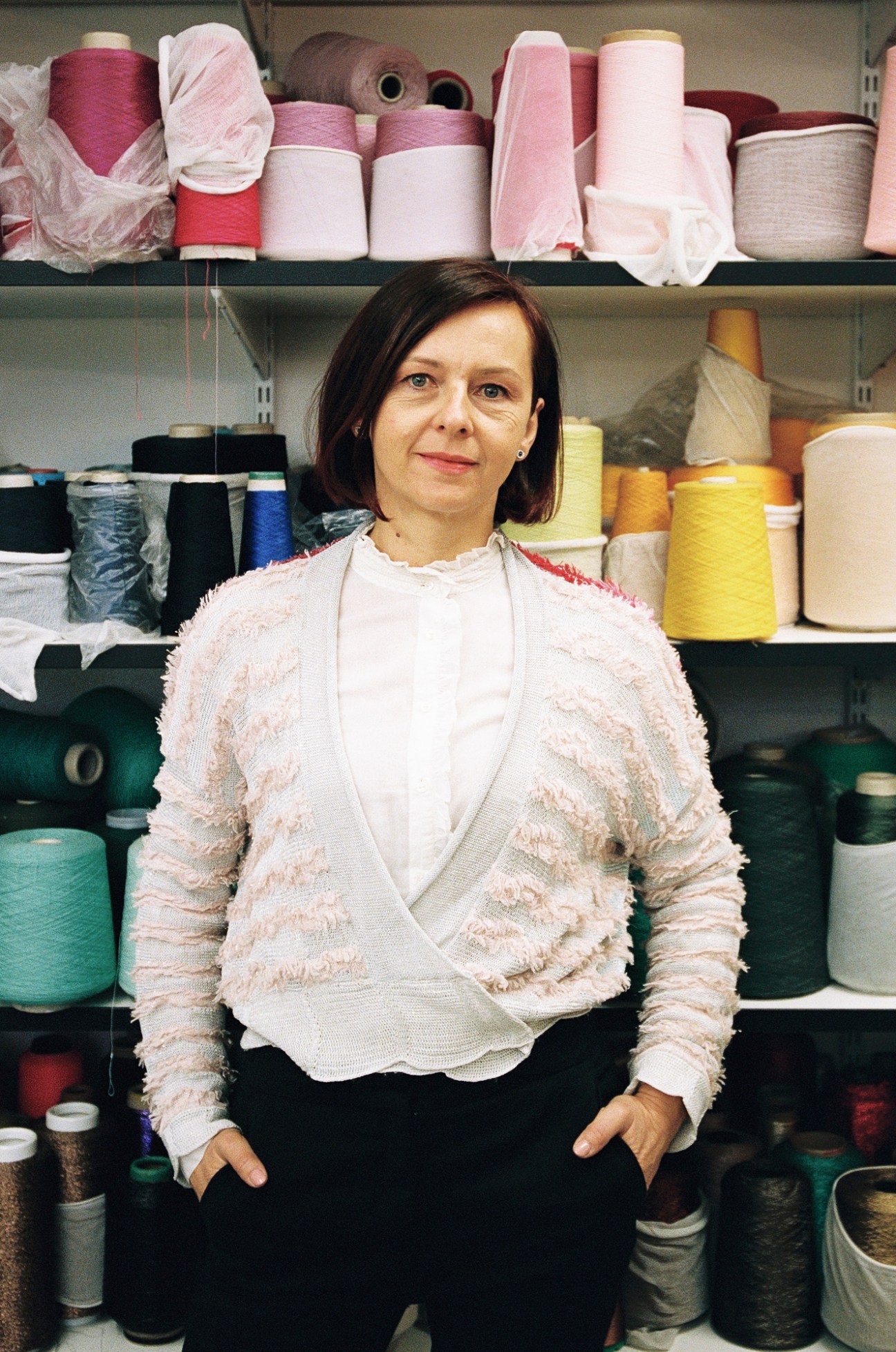 Tanja Uvera, fashion designer, standing in her studio surrounded by colorful spools of thread and fabric