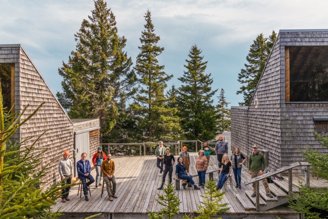 Team members of Haystack Mountain School of Crafts standing together on wooden deck surrounded by cedar buildings