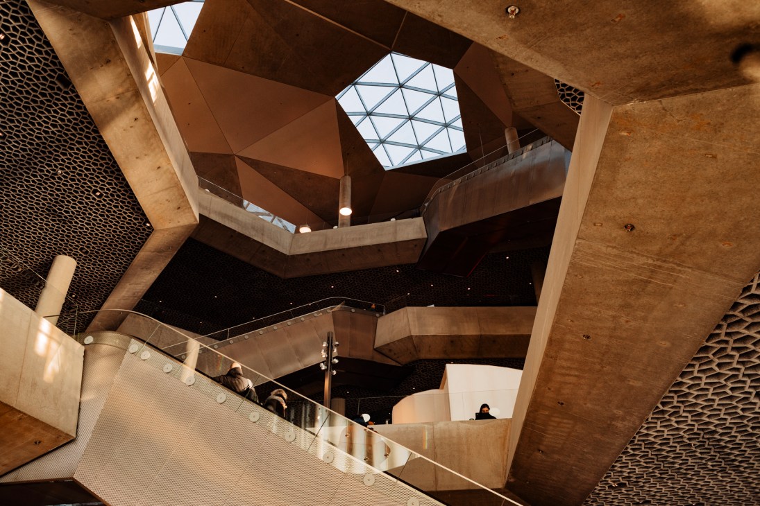 Interior view of modern library showing wooden architectural elements, hexagonal skylights, and curved staircase