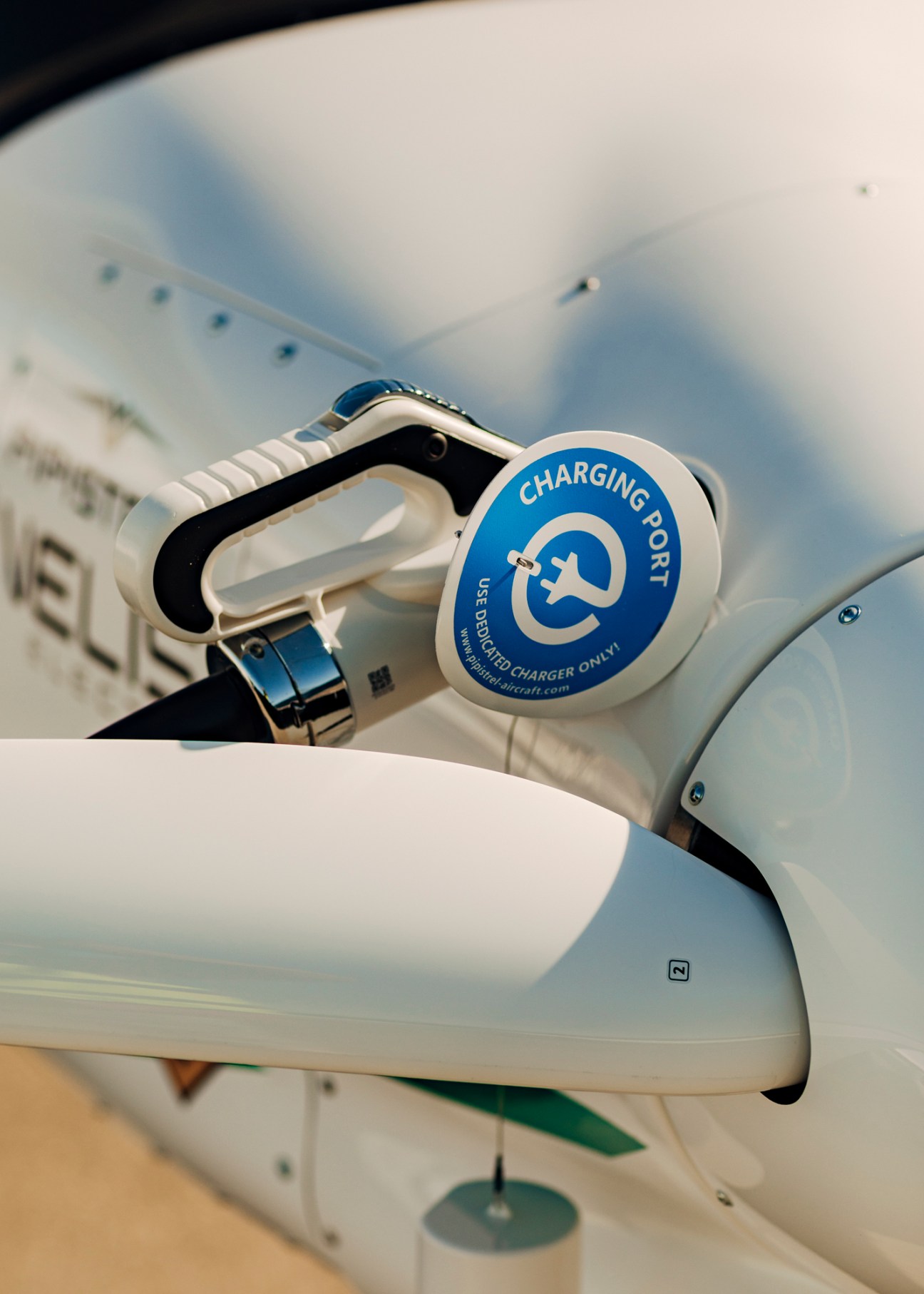 Person connecting charging cable to white electric aircraft with blue charging port label