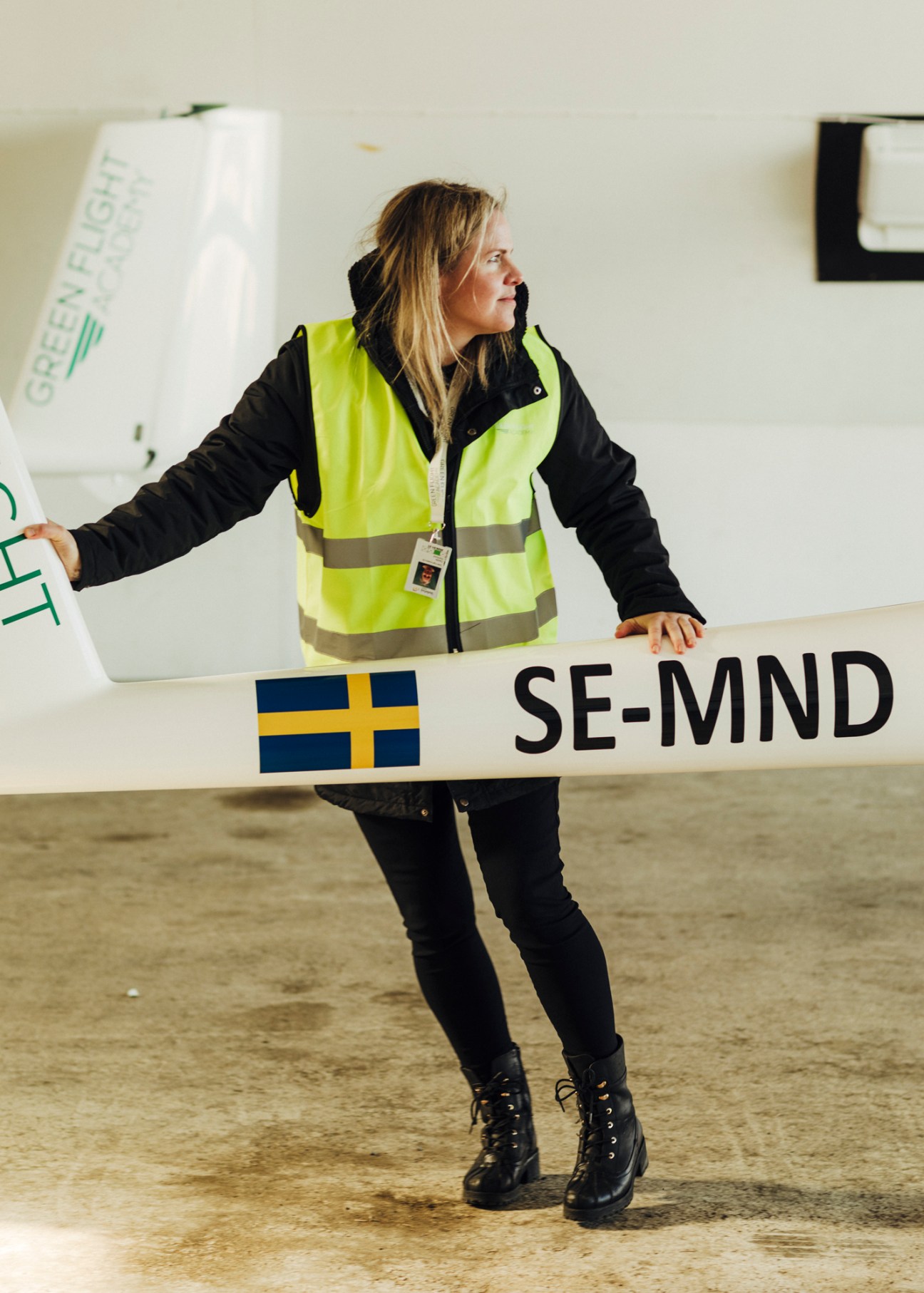 Woman in high-visibility safety vest maneuvering aircraft wing in hangar, with SE-MND registration visible