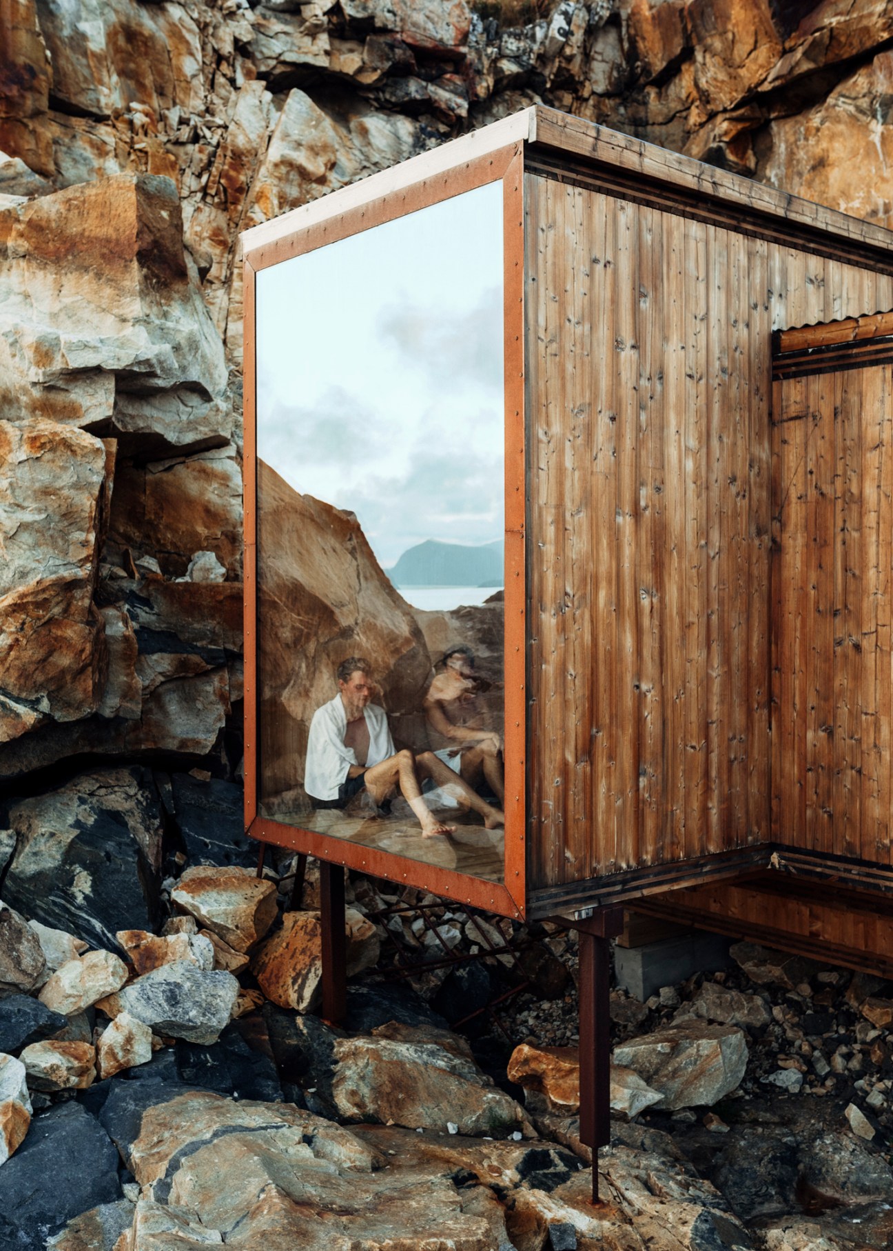 Timber-and-glass panoramic sauna by Oslotre built into rocky cliffs overlooking the sea in Lofoten, Norway.