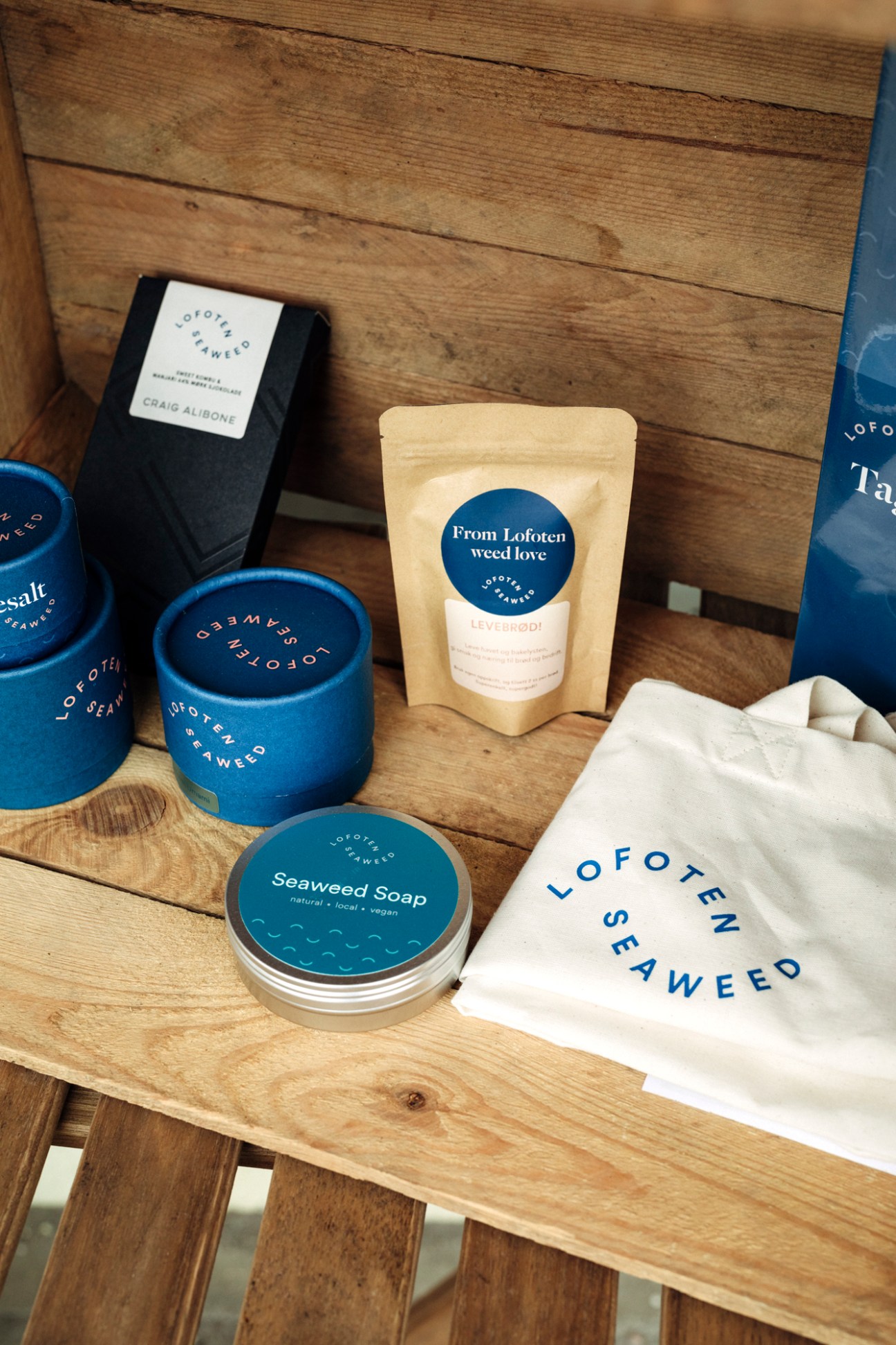 Lofoten Seaweed products including blue ceramic containers, black packaging, kraft paper pouch, seaweed soap, and branded cloth bag displayed on wooden surface.