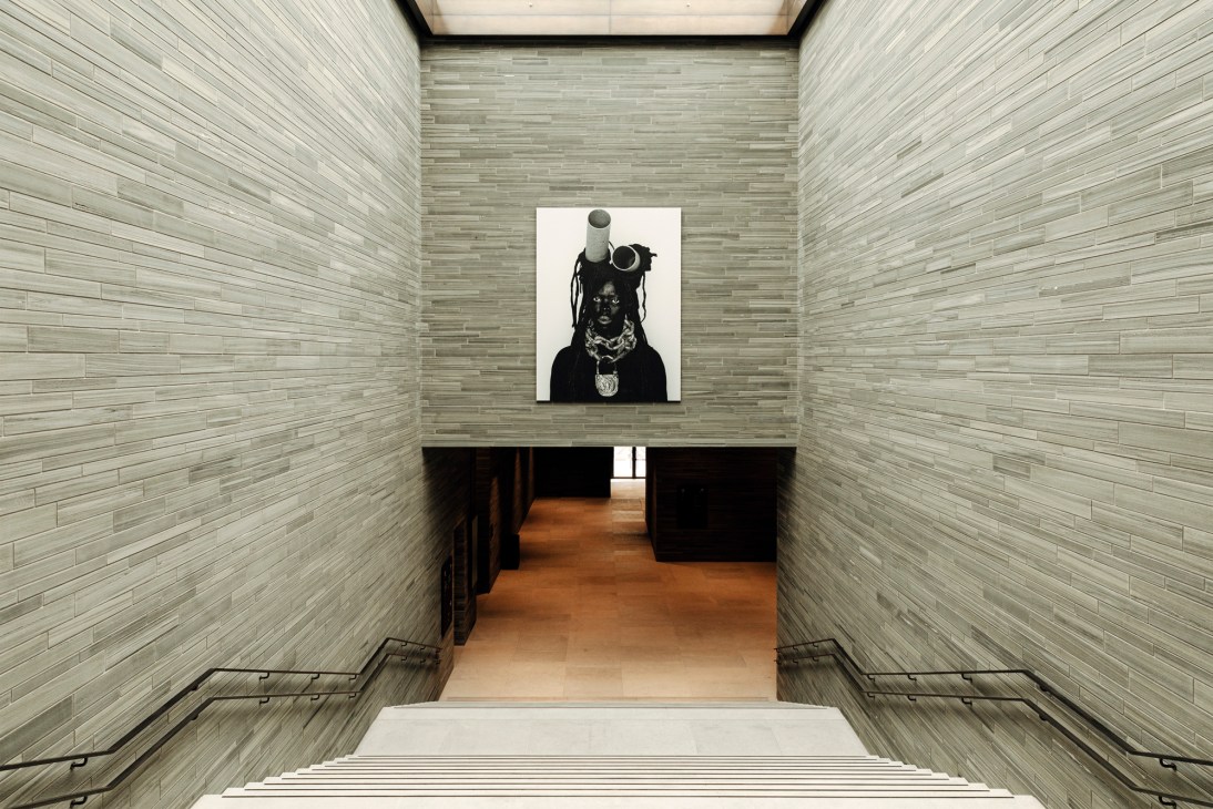 Black and white portrait photograph displayed in a minimalist gallery space with pale brick walls.