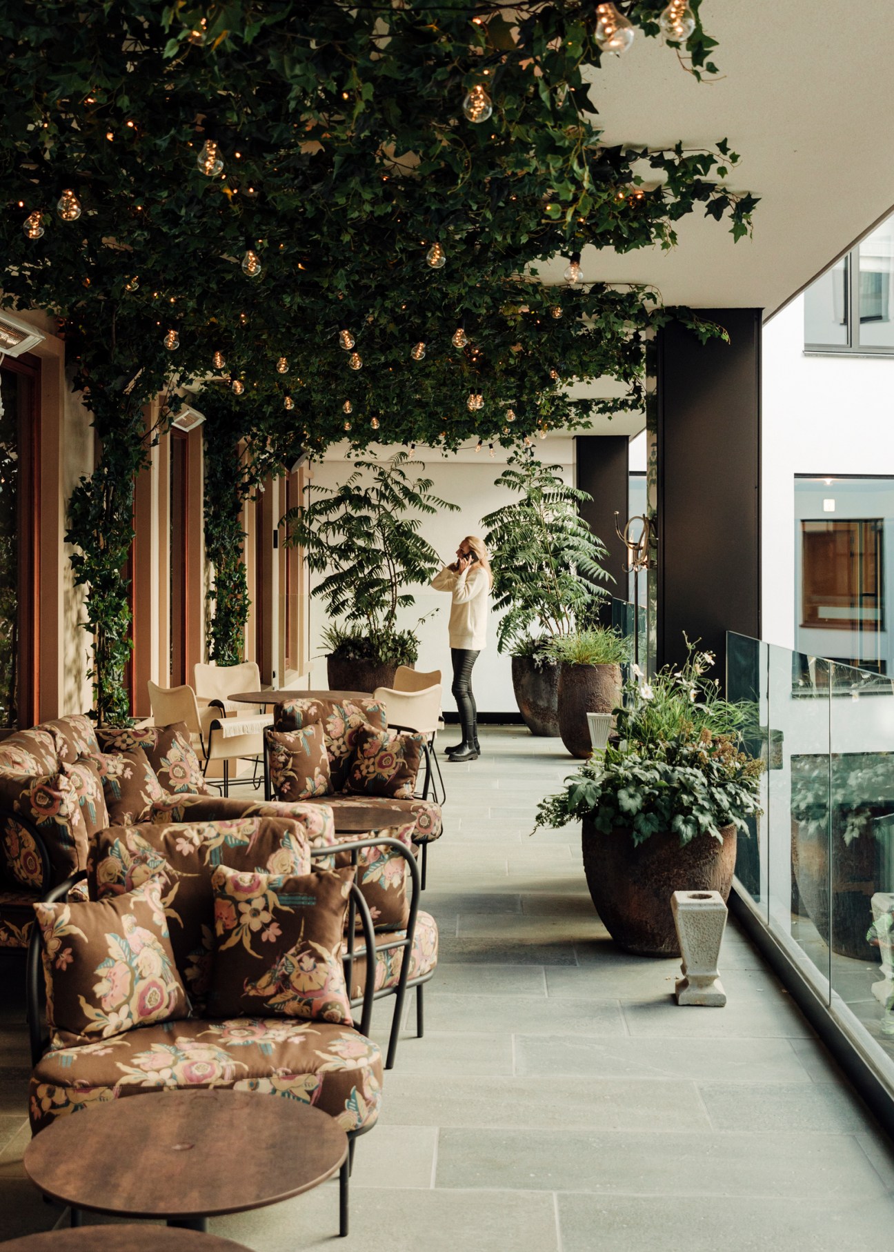 Sommerro hotel interior with floral armchairs, string lights overhead, and lush plants in an atrium-style space